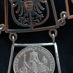 Bildausschnitt zeigt die rückwärtigen Glieder der Amtskette mit Gelnhäuser Wappen und einer Münze mit dem Abbilkd von Kaiser Barbarossa.