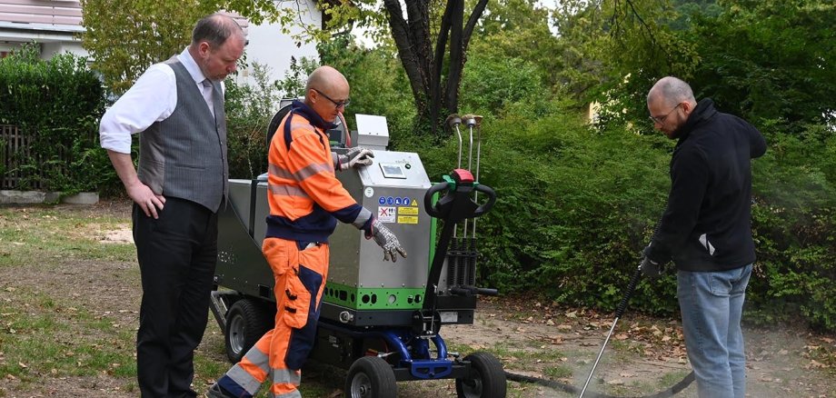 Bürgermeister und Mitarbeiter des Betriebshofs testen das Heißwasser-Dampf-Gerät auf dem Spielplatz in Meerholz.