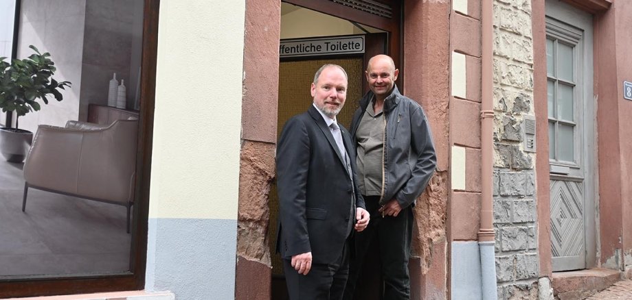 Bürgermeister Christian Litzinger und Projektleiter Thorsten Amend stehen im Eingang der neuen öffentlichen Toilette an der Kuhgasse.