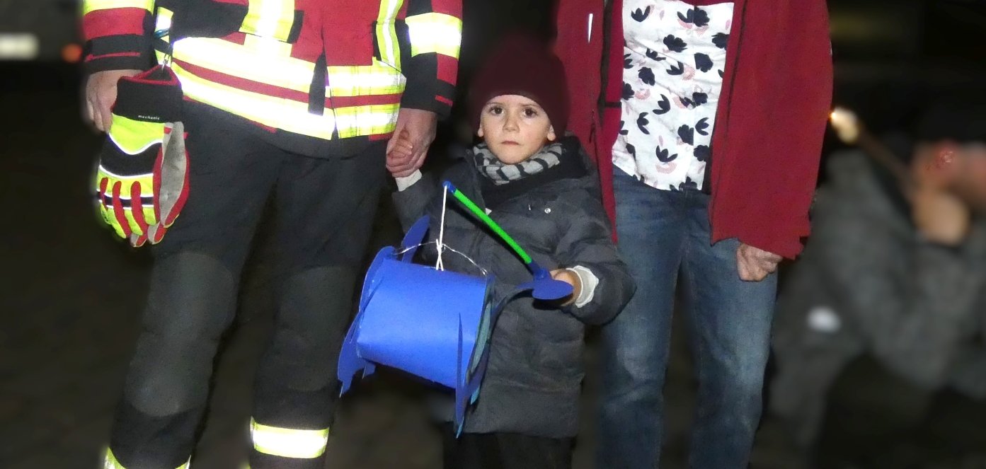 Ein Feuerwehrmann und ein Kind mit Laterne sowie eine erwachsene Frau.