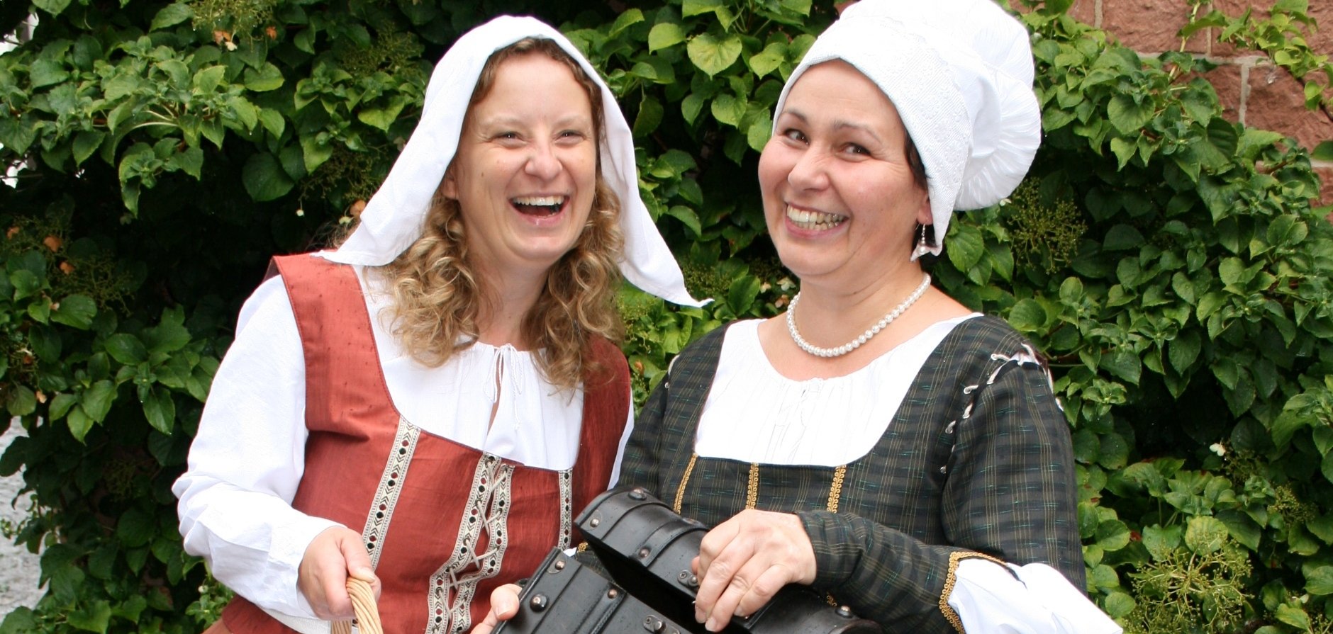 Zwei fröhliche Gästeführerinnen mit mittelalterlichen Utensilien.