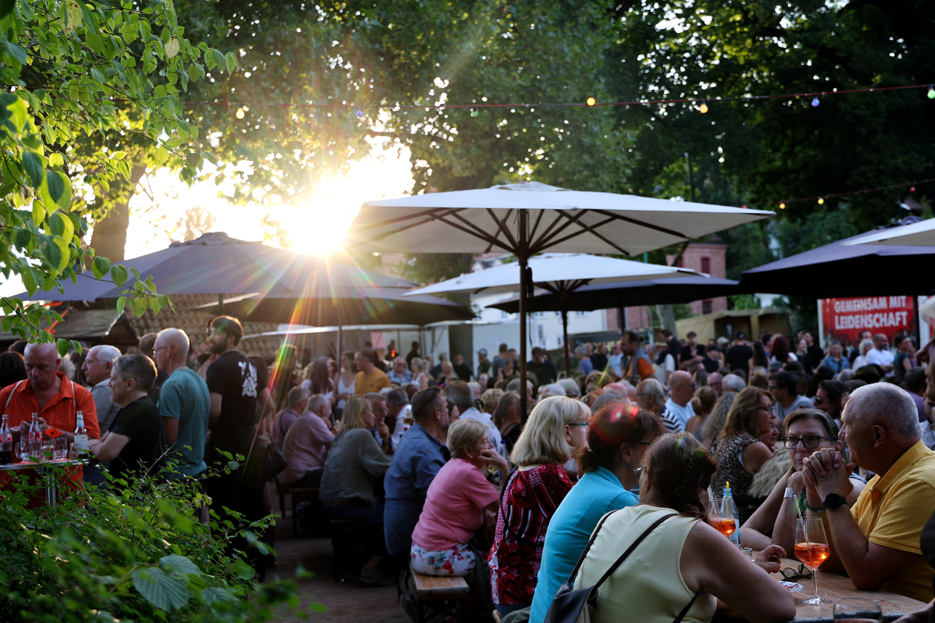 Menschenmassen sitzen an Tischen im Stadtgarten und Essen und Trinken. 