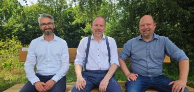 Der Bürgermeister und EAM-Vertreter sitzen auf der neuen Bank auf der Müllerwiese.
