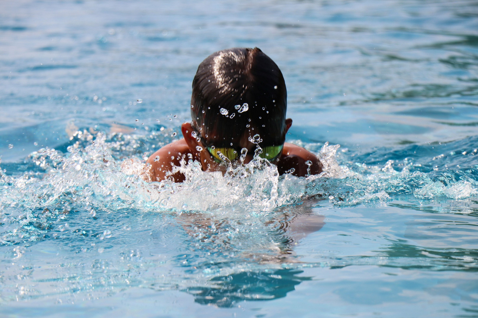 Freibad Gelnhausen Ein Junge mit moderner Chlorbrille beim Schwimmen. Vor ihm spritzt Wasser auf.