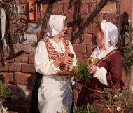 Gaumenkützel Zwei lachende Frauen in historischen Gewändern vor einer Sandsteinmauer.