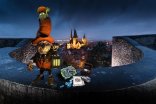 Gelnhusana magica Ein Kobold mit roter Mütze und Laterne steht in der Dämmerung auf der Stadtmauer. Im Hintergrund sind die beleuchteten Türme der Marienkirche zu sehen.