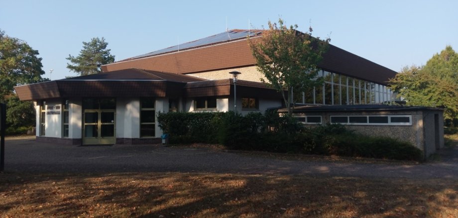 Man sieht ein Gebäude mit einem Achteckigen Anbau. Das Gebäude hat eine Große Fensterfront und es wachsen einige Bäume im Hof des Gebäudes.  