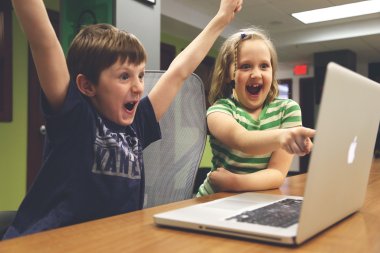 Zwei kinder sitzen am Computer und jubeln.