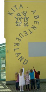 Kita Abenteuerland Bild der Außenwand der Kita Abenteuerland mit dem Logo und fünf Kindern darunter