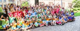 Gruppenbild vom Kindersommer. Alle haben bunte T-Shirts an und ihre Arme nach oben gestreckt.