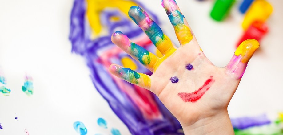 Bild einer kleinen Kinderhand die mit Fingerfarben in verschiedenen Farben malt