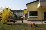Kita Roth Bild des Spielplatzes der Kita Roth mit Holzbänken und einem roten Dreirad auf der Wiese.