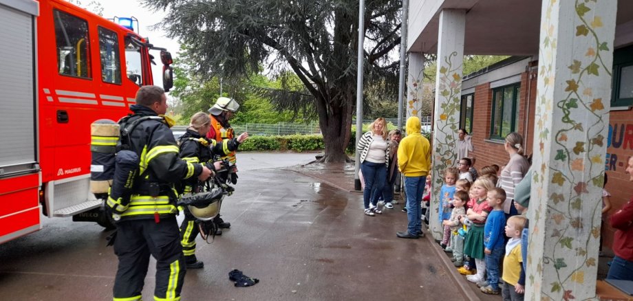 Drei Einsatzkräfte der Feuerwehr geben den Kindern Anweisungen. 