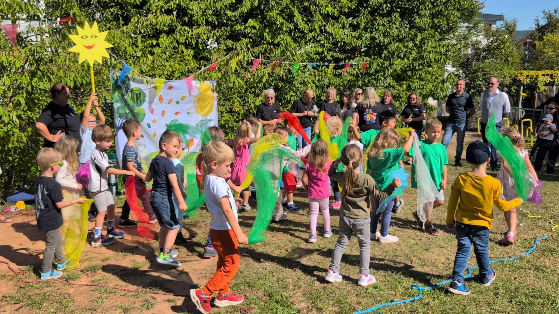Kinder und Erwachsene feiern zusammen auf einer Wiese das Jubiläumsfest der Kita "Freche Früchtchen".