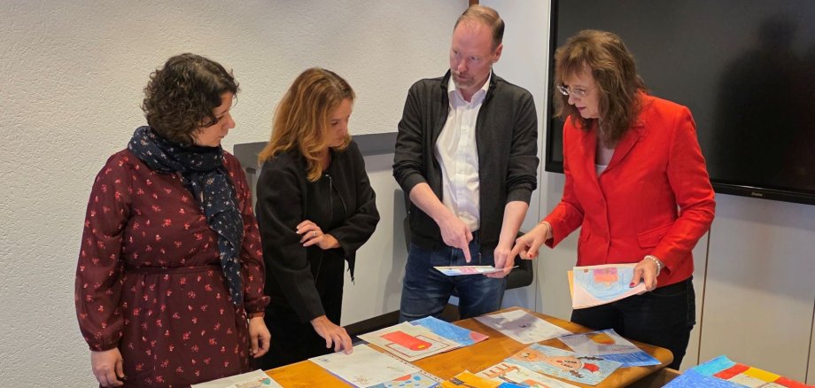 329 Kinder malen bunte Bilder für die Weihnachtsstadt Gelnhausen Vier Personen stehen im Sitzungssaal im Rathaus um einen Tisch herum und suchen die schönsten gemalten Bilder für den Riesenadventskalender in Gelnhausen aus.