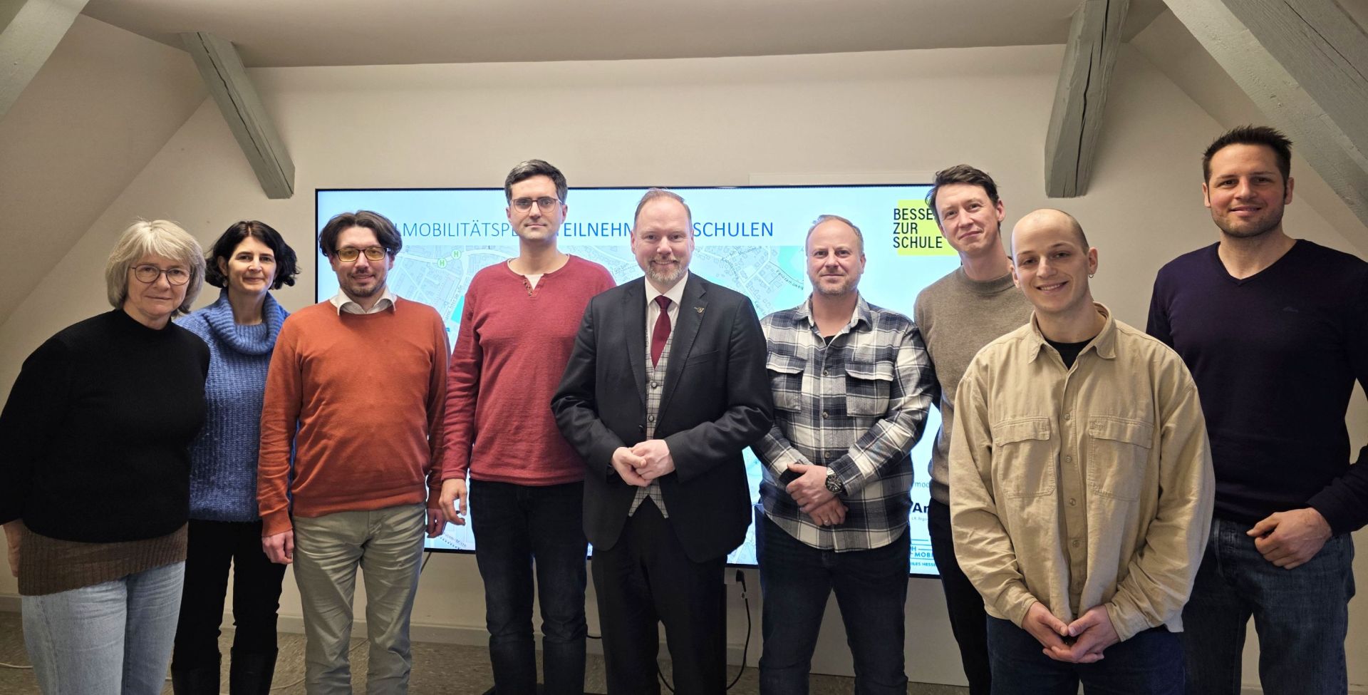 Eine Gruppe Personen steht in einem Raum vor einem Bildschirm. 