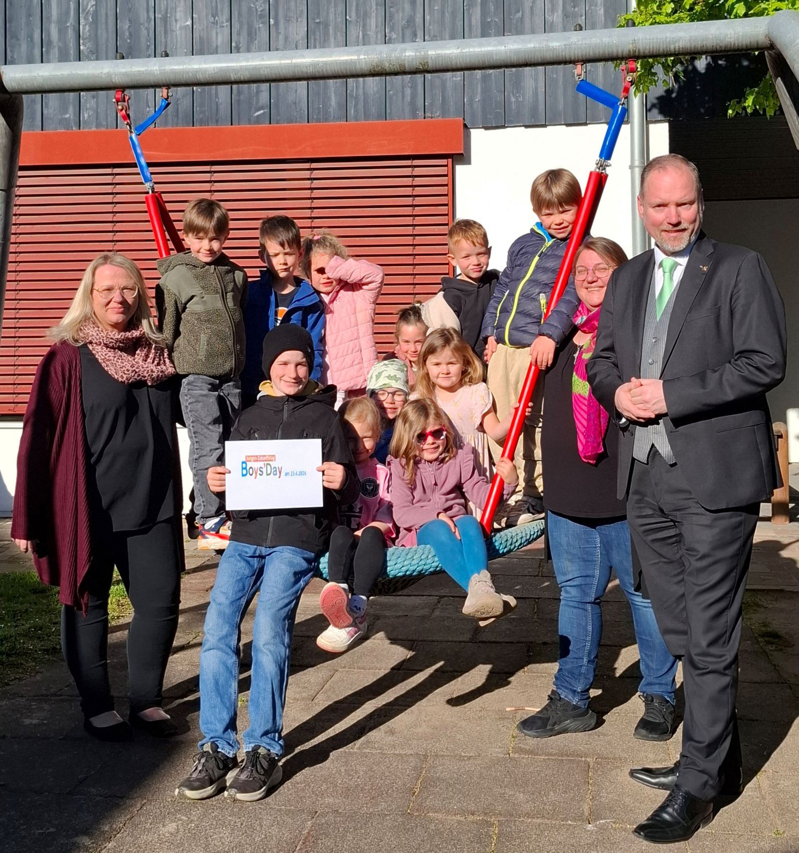 Bürgermeister Christian Litzinger steht mit zwei Frauen vom Kita-Team und mehreren Kindern vor der Kita „Freche Früchtchen“ draußen an einer Schaukel mit dem Praktikanten Gideon.
