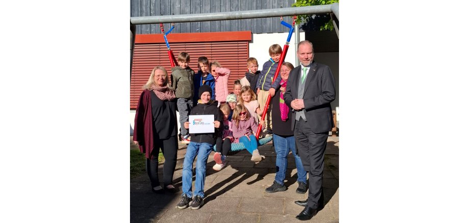 Bürgermeister Christian Litzinger steht mit zwei Frauen vom Kita-Team und mehreren Kindern vor der Kita „Freche Früchtchen“ draußen an einer Schaukel mit dem Praktikanten Gideon.