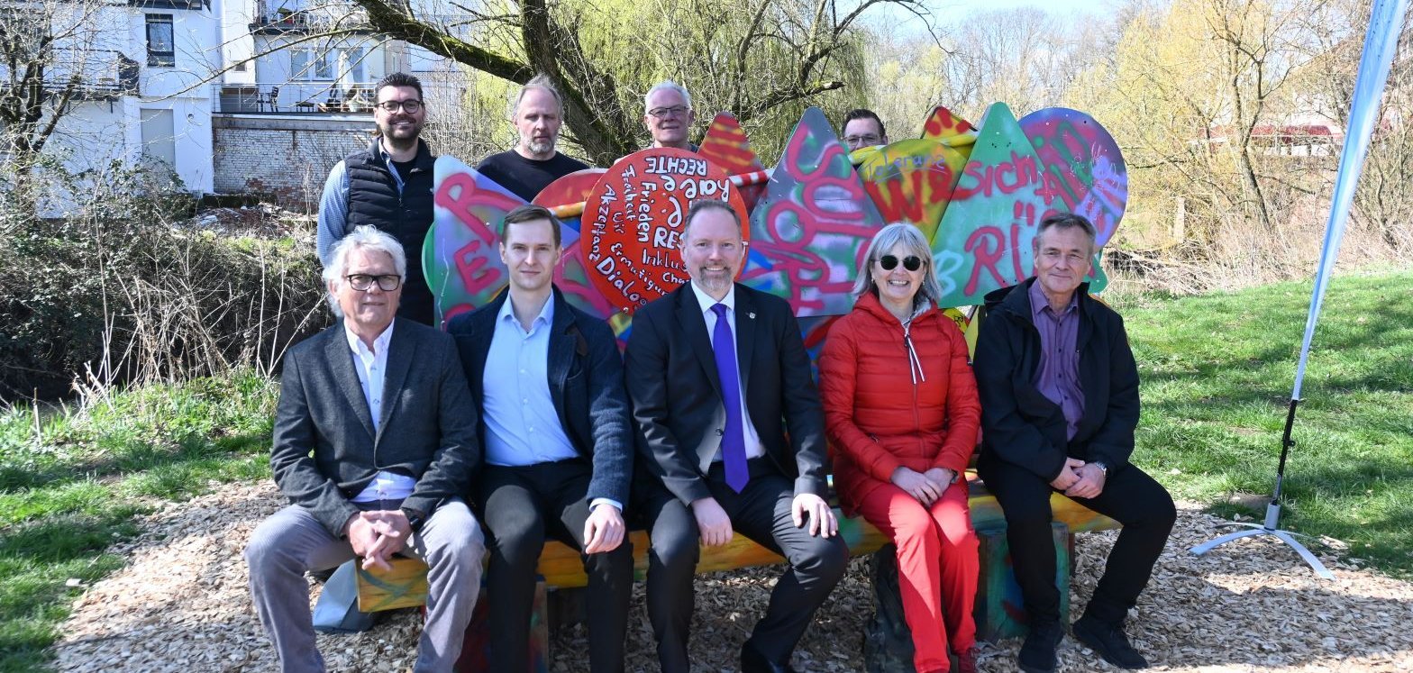 Die Projektunterstützer sitzen auf und stehen bei der Bank auf der Müllerwiese, die eine Graffiti-Kunstinstallation ist. 