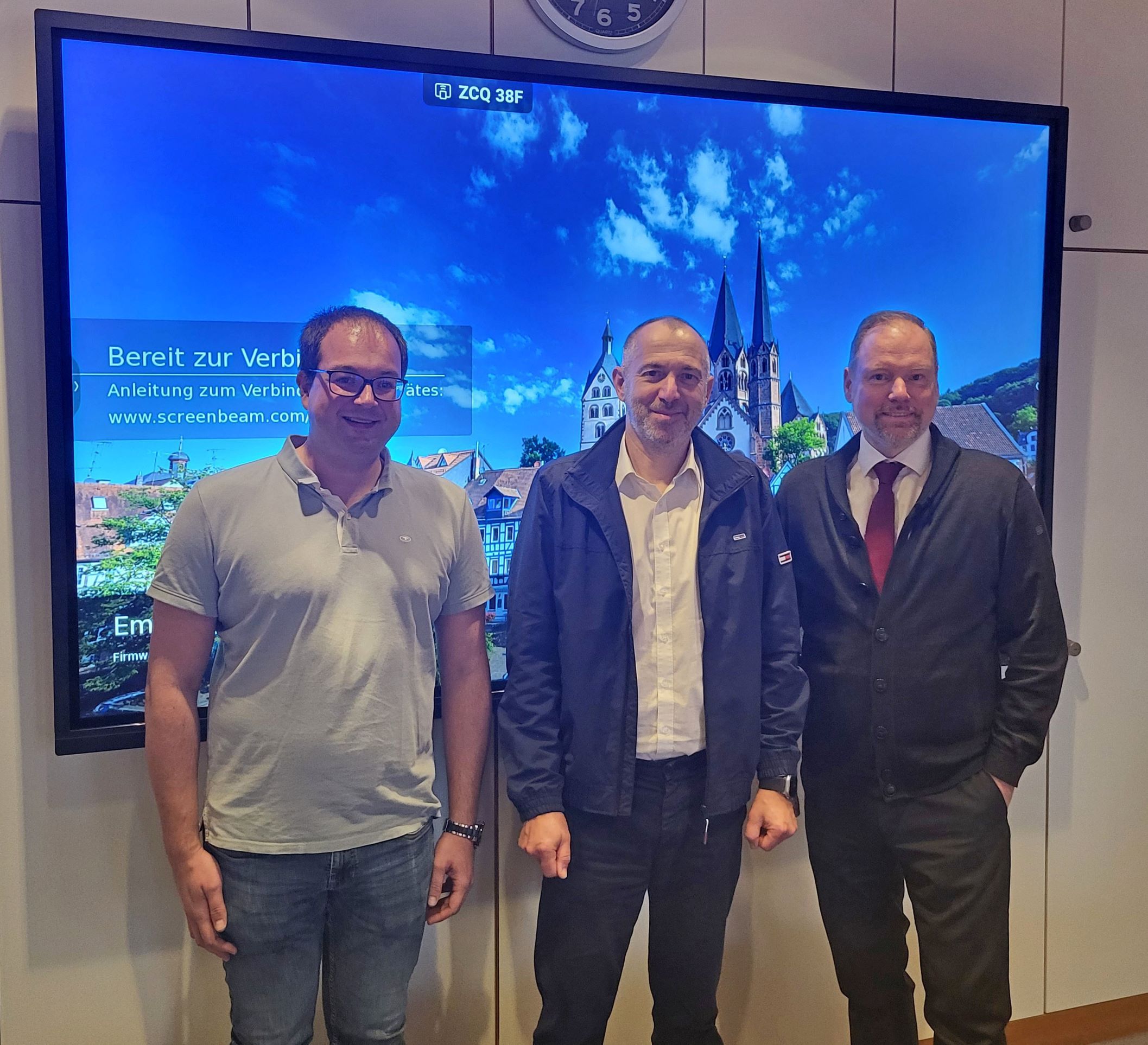 Bürgermeister Christian Litzinger, de-bit Geschäftsführer Jörg Deusinger und Digitalisierungsbeauftragter der Stadt Gelnhausen Dennis Naumann stehen im Sitzungssaal im Rathaus vor einem Großbildfernseher.