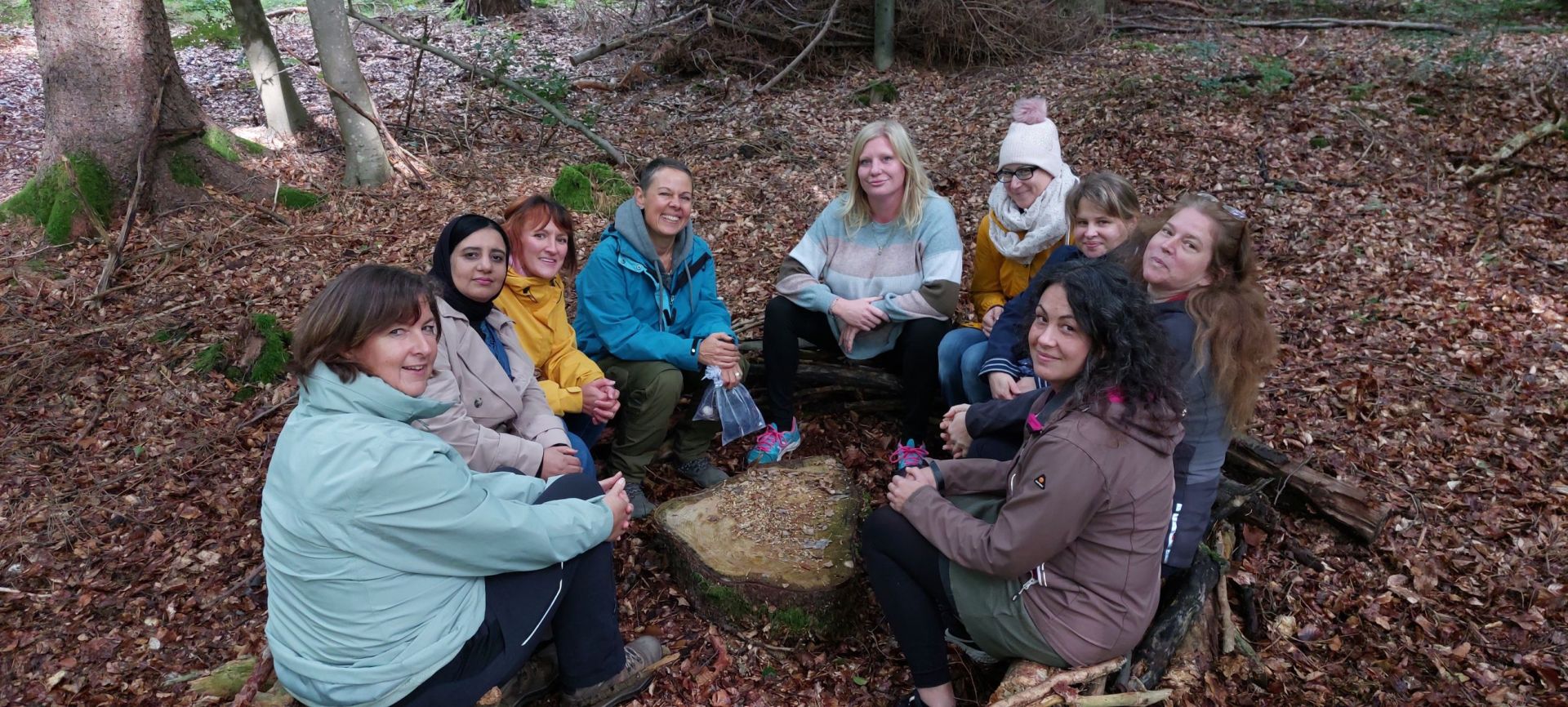 Tagespflegepersonen sitzen auf Holzstämmen im Kreis im Wald.