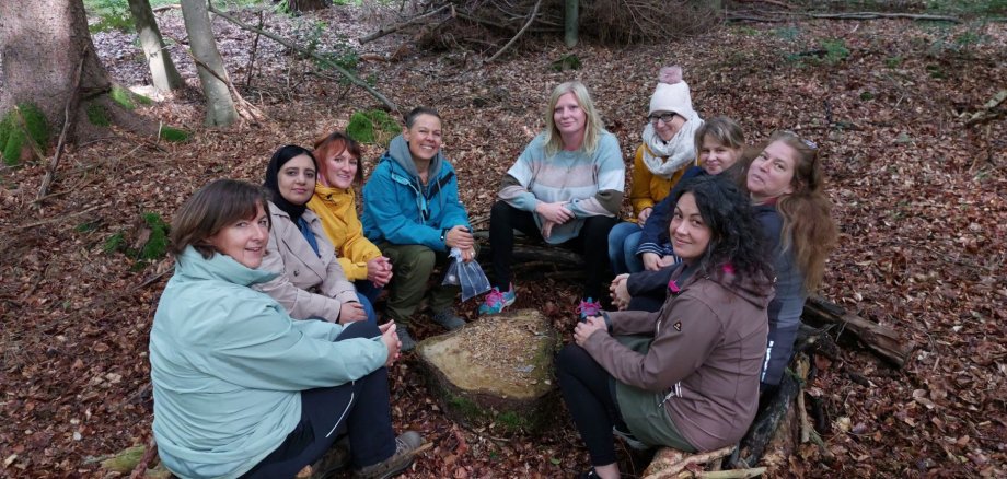 Tagespflegepersonen sitzen auf Holzstämmen im Kreis im Wald.