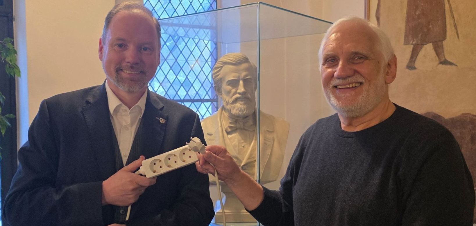 Bürgermeister Christian Litzinger (links) und Stadtrat Bernd Wietzorek (rechts) stehen gemeinsam im Rathausfoyer mit dem Plakat der "Earth Hour" 2026 und laden zum Mitmachen ein. 