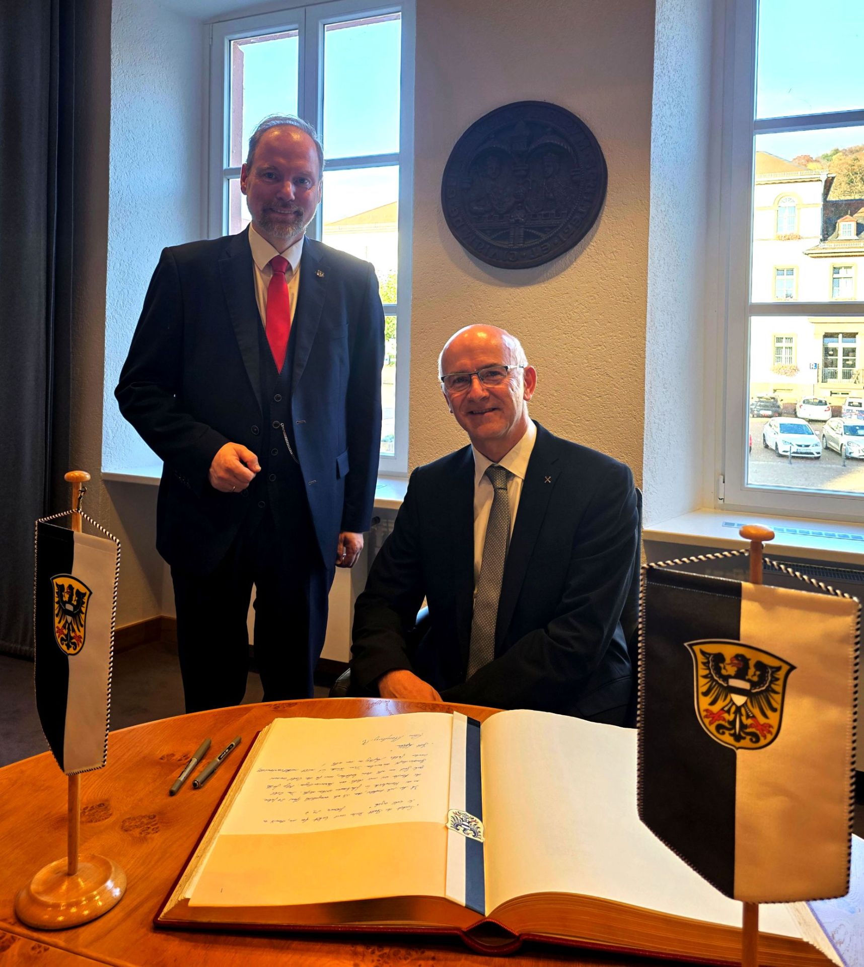 Pfarrer Rainer Schomburg sitz im Sitzungssaal des Rathauses vor einem Tisch auf dem das Goldene Buch der Stadt Gelnhausen liegt. Bürgermeister Christian Litzinger steht neben ihm. 