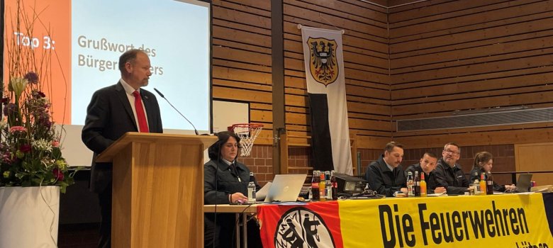 Bürgermeister Christian Litzinger steht an einem Podium in einer Halle und eröffnet die Versammlung. 