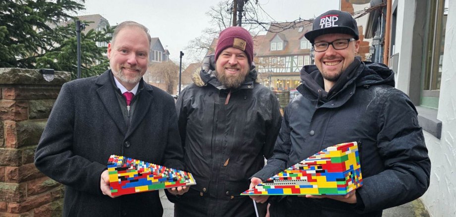 Der Bürgermeister steht mit zwei Männern an der Treppe zur Terrasse am Untermarkt. Die beiden Männer Teile von Legorampen in den Händen. 