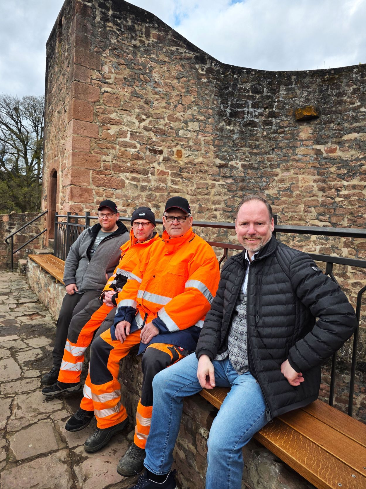 Bürgermeister Christian Litzinger (rechts) und die Mitarbeiter des städtischen Betriebshofs, darunter der stellvertretende Betriebshofleiter Andreas Schleich (links), sitzen auf der neuen Sitzbank am Halbmond im Stadtgarten Gelnhausen.  