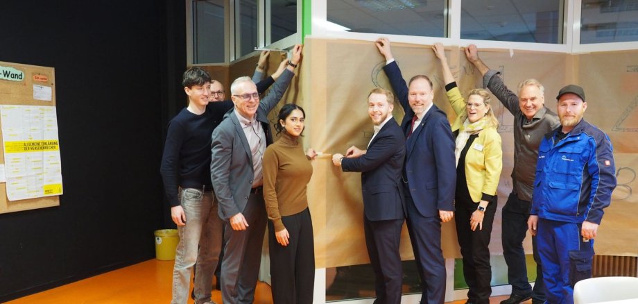 Neues Selbstlernzentrum eröffnet Eine Gruppe Menschen entfernt zur Eröffnung gemeinsam die Abdeckung am Eingang des neuen Selbstlernzentrums.