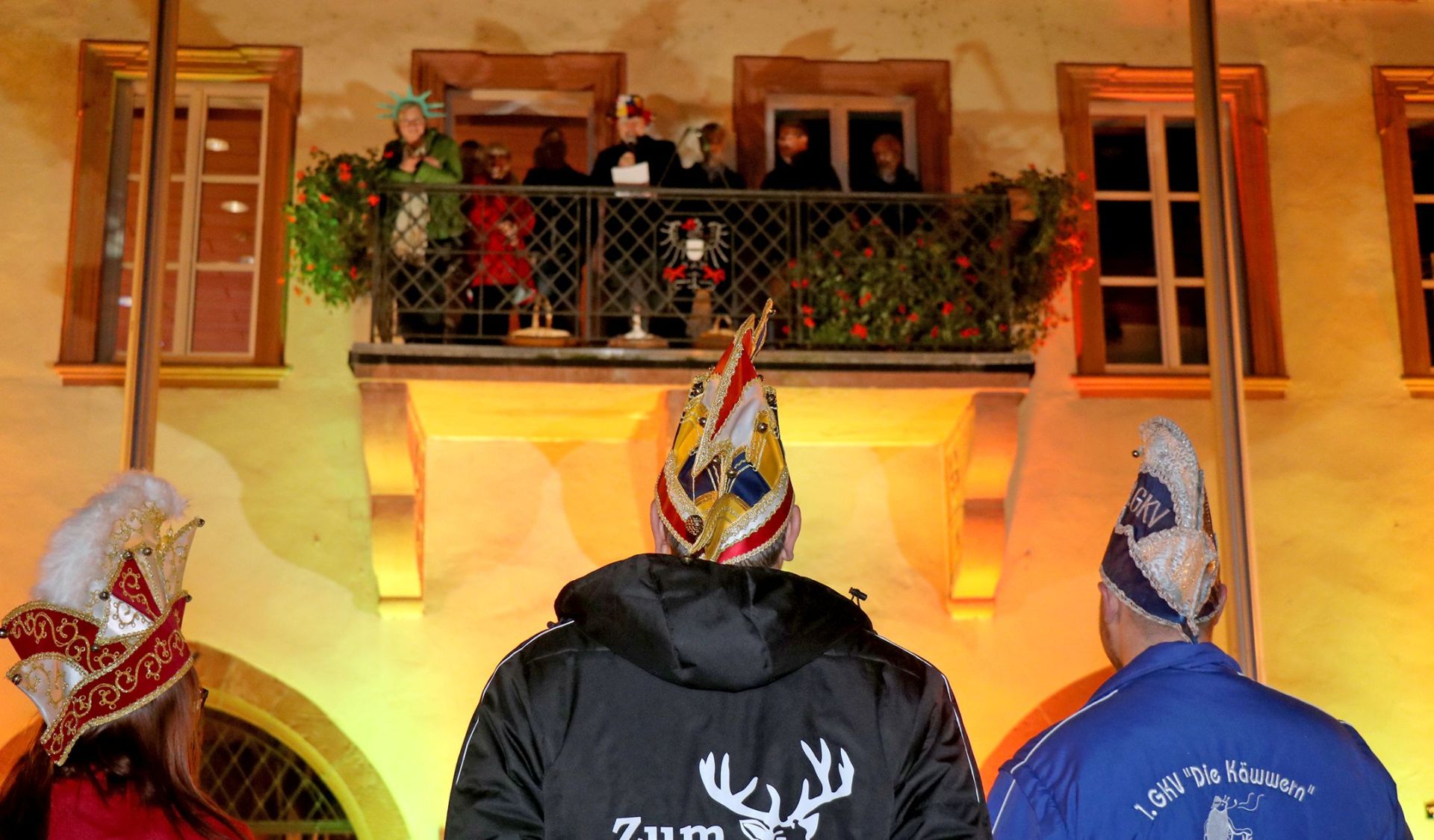 Mitglieder der Karnevalsvereine stehen vor dem Rathaus und schauen auf den Balkon hinauf, auf dem Mitglieder des Magistrats stehen.