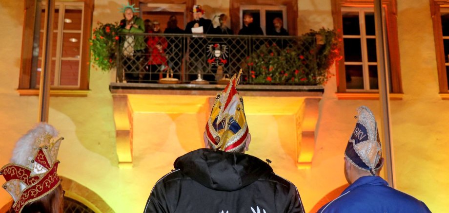 Rathaussturm 2024 Mitglieder der Karnevalsvereine stehen vor dem Rathaus und schauen auf den Balkon hinauf, auf dem Mitglieder des Magistrats stehen.