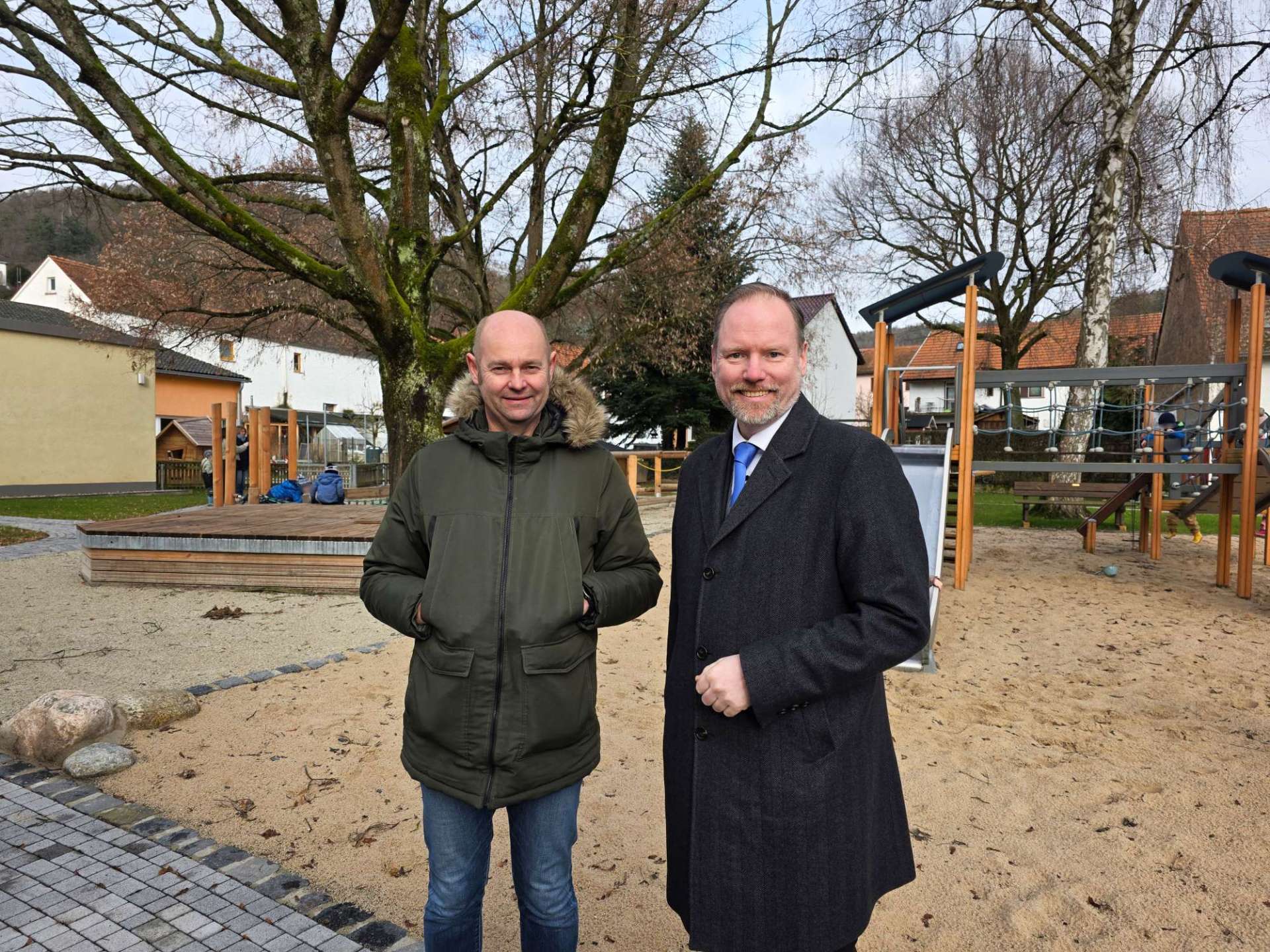 Bürgermeister Christian Litzinger (rechts) und Projektleiter Thorsten Amend (links) stehen auf dem neugestalteten Außengelände der Kita „Röther Gickel“. 