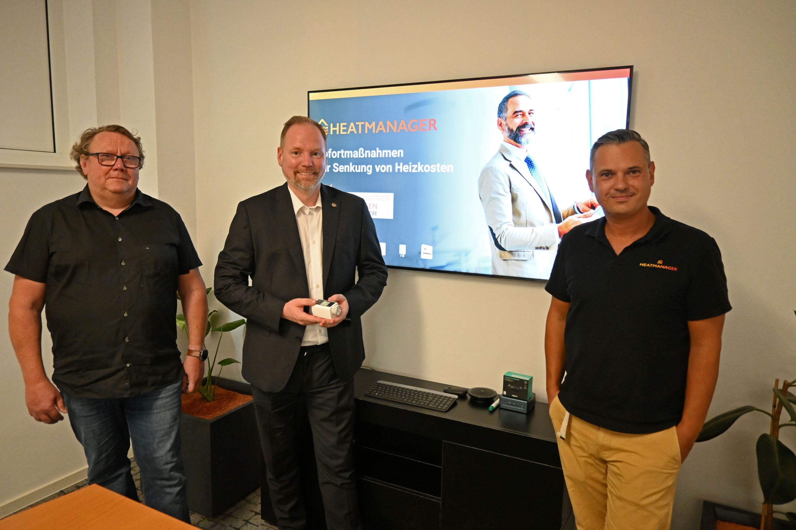 Die Heatmanager-Geschäftsführer Stefan Luther und Steffen Matheis stehen mit Bürgermeister Christian Litzinger in einem Büroraum vor einem Bildschirm. 