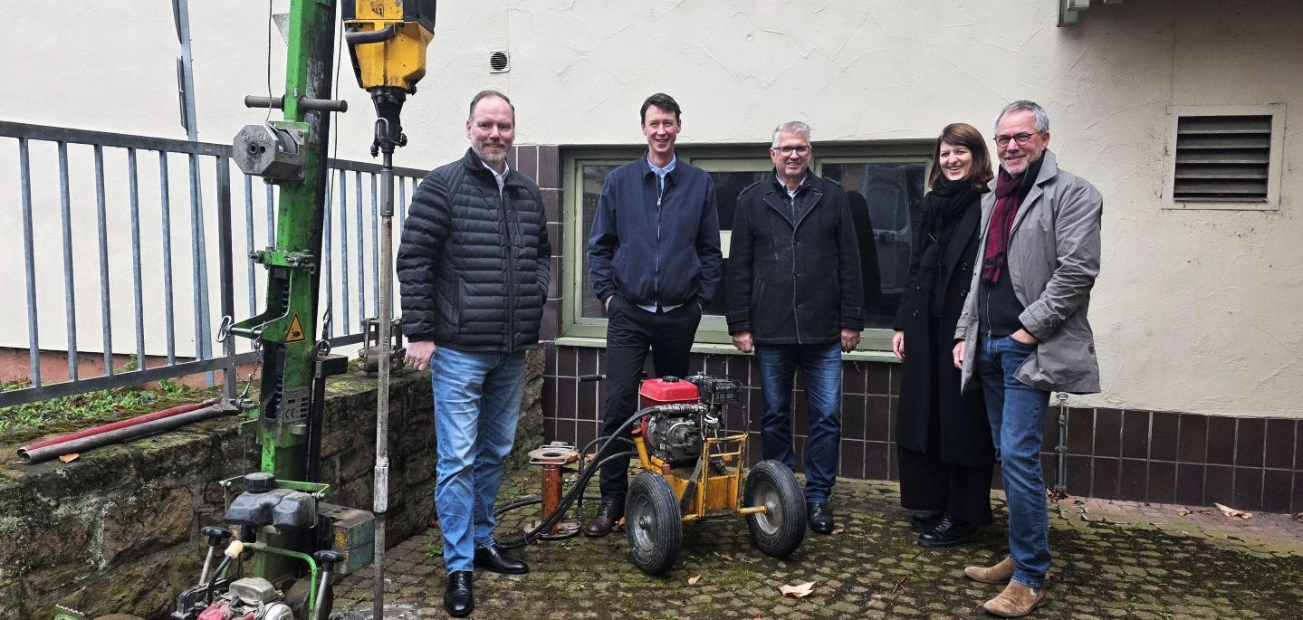 Fünf Personen stehen vor der Stadthalle in einem Hof, neben ihnen zwei große Bodenbohrer.