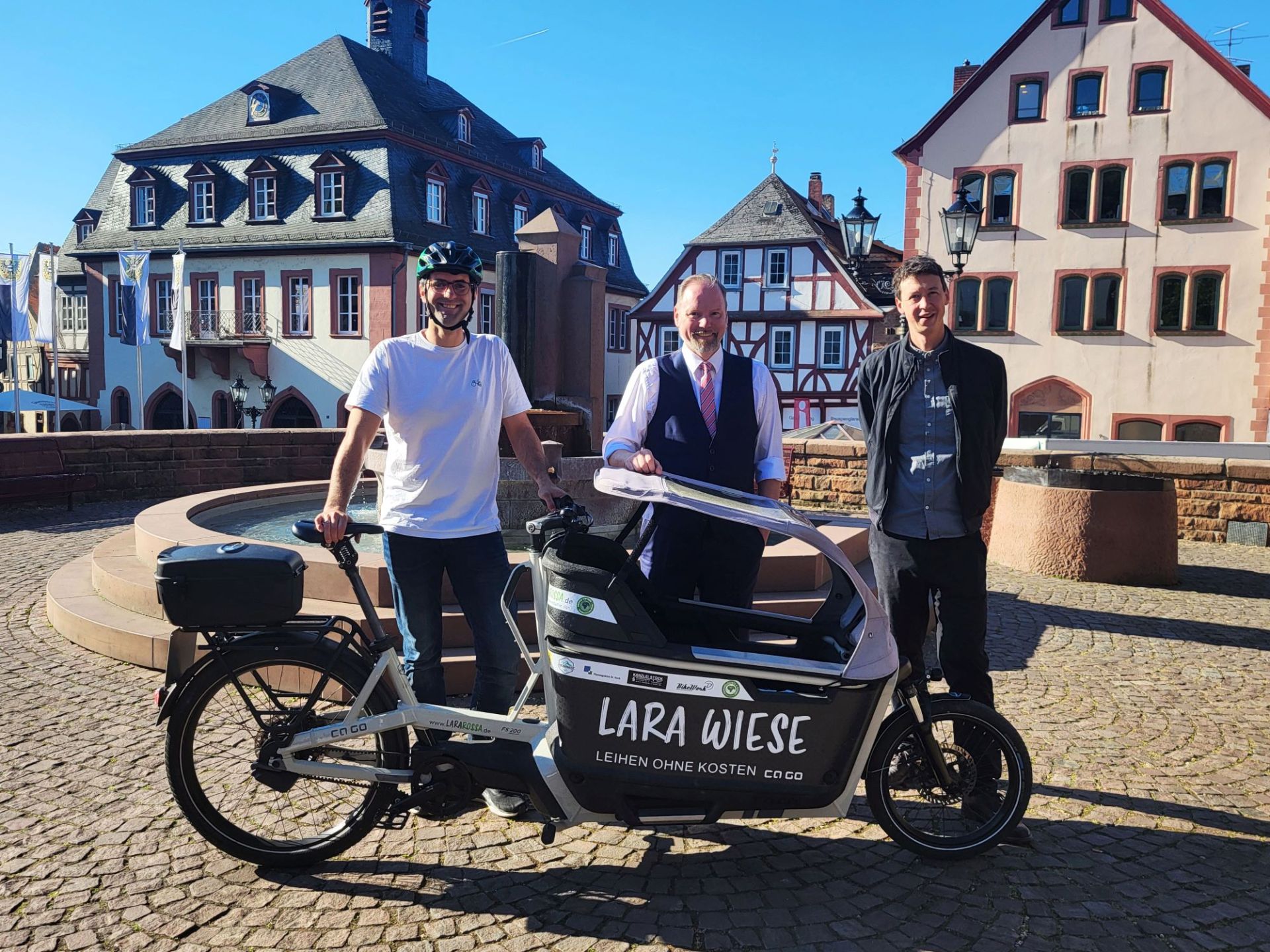 Klimamanager Andreas Hlasseck, Bürgermeister Christian Litzinger und Bauamtsleiter Eppo Haas stehen mit einem Fahrrad auf dem Obermarkt in Gelnhausen.