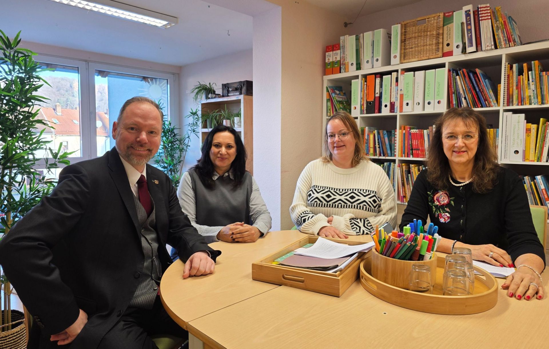 Vier Personen sitzen in einer Kita um einen Tisch herum. 