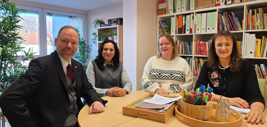 Vier Personen sitzen in einer Kita um einen Tisch herum. 