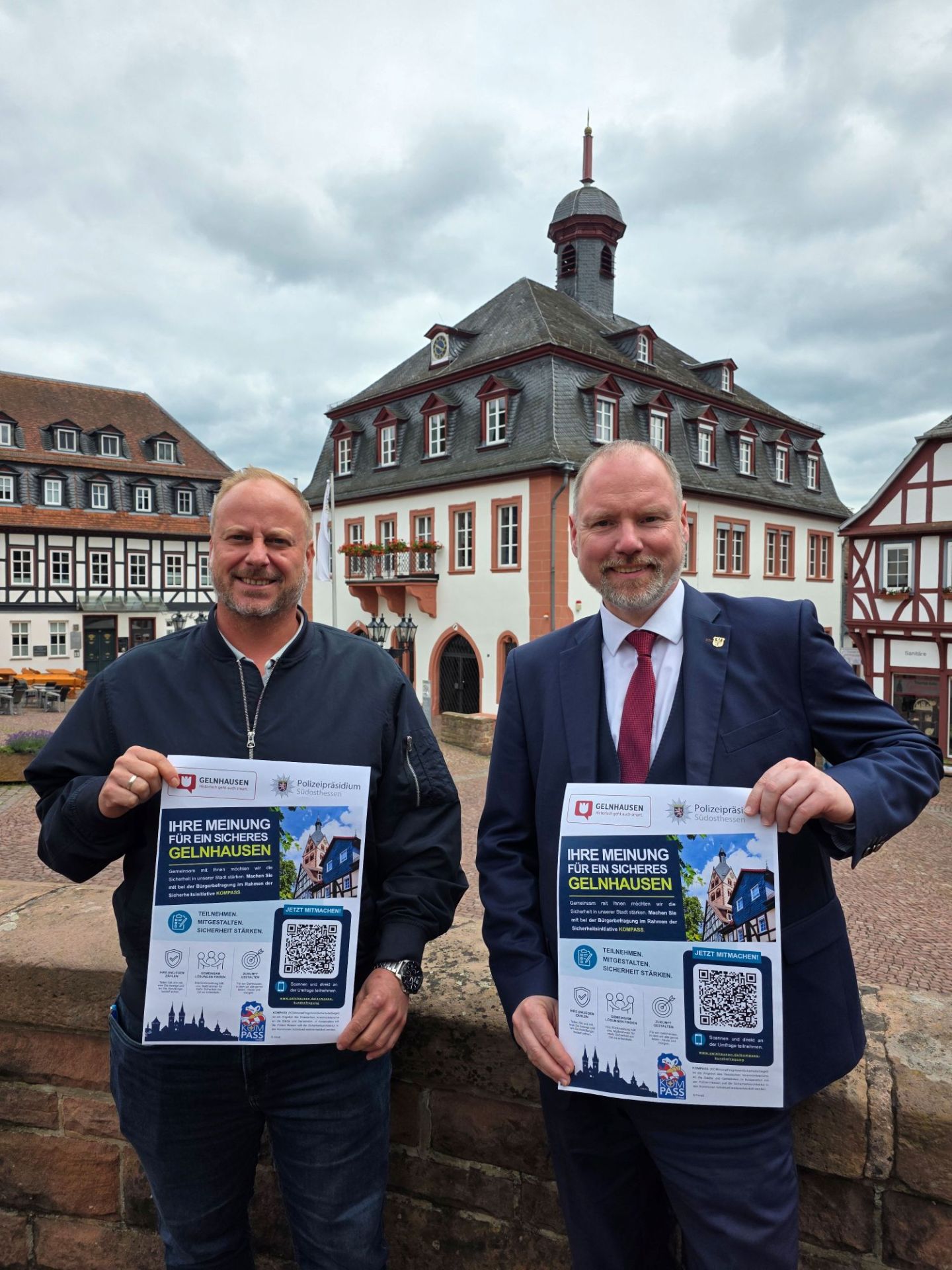 Bürgermeister Christian Litzinger (rechts) und Ordnungsamtsleiter Bastian Metzler (links) stehen auf dem Obermarkt und halten jeweils ein Plakat in die Kamera, das zur Teilnahme an der KOMPASS-Kurzbefragung aufruft.