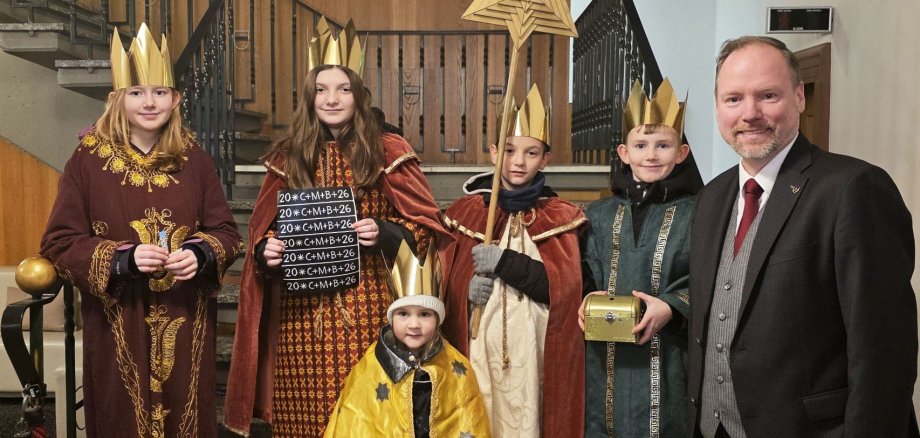 Bürgermeister Christian Litzinger und fünf Kinder als Sternsinger verkleidet stehen zusammen im Foyer des Rathauses in Gelnhausen. 