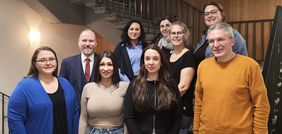 9 Personen stehen im Rathaus an und auf einer Treppe.