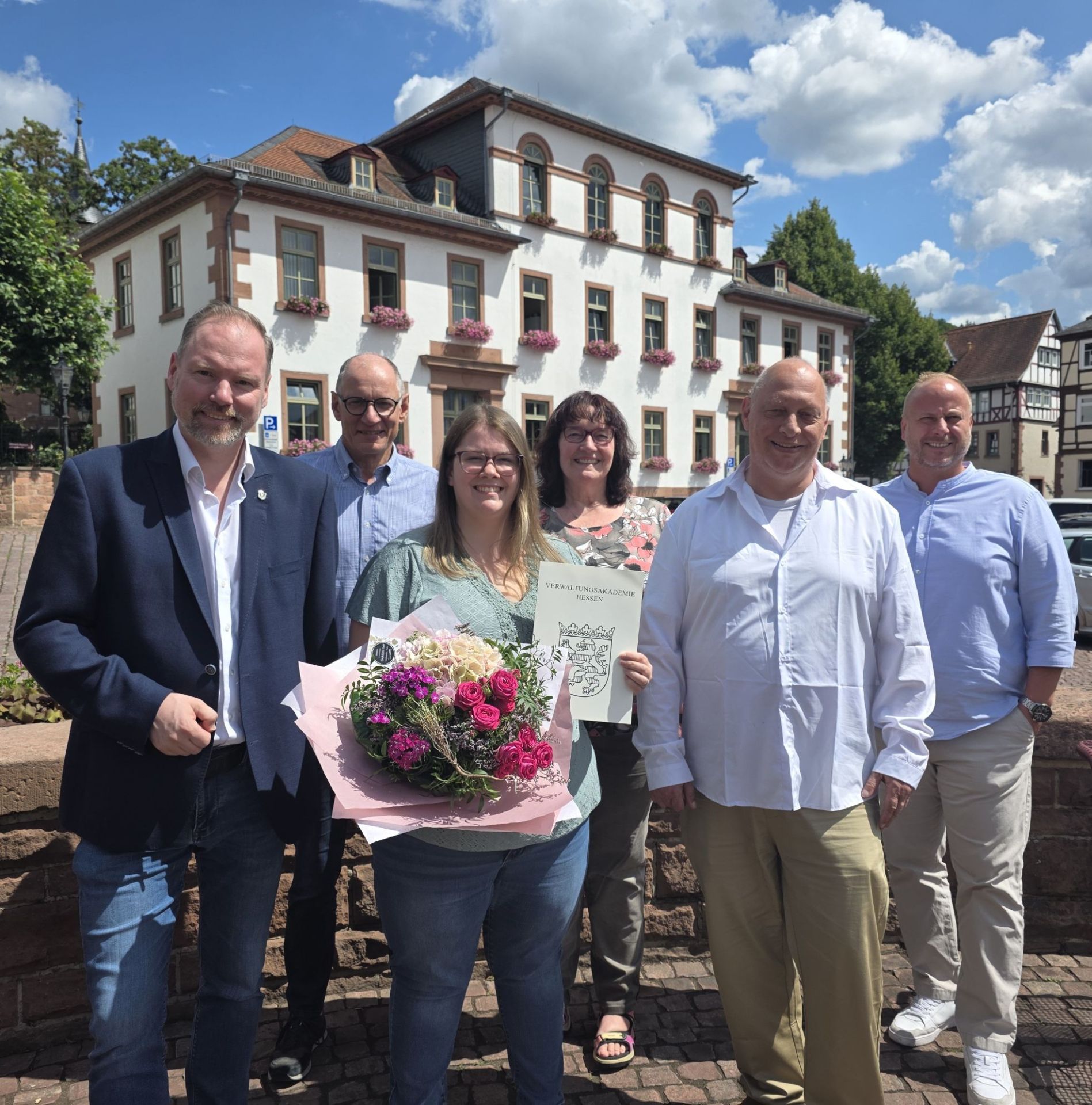 Bürgermeister Christian Litzinger, Ausbildungsabsolventin Lea Mohn und Mitarbeiterinnen und Mitarbeiter des Rathauses stehen auf dem Obermarkt vor der alten Bürgerschule. 