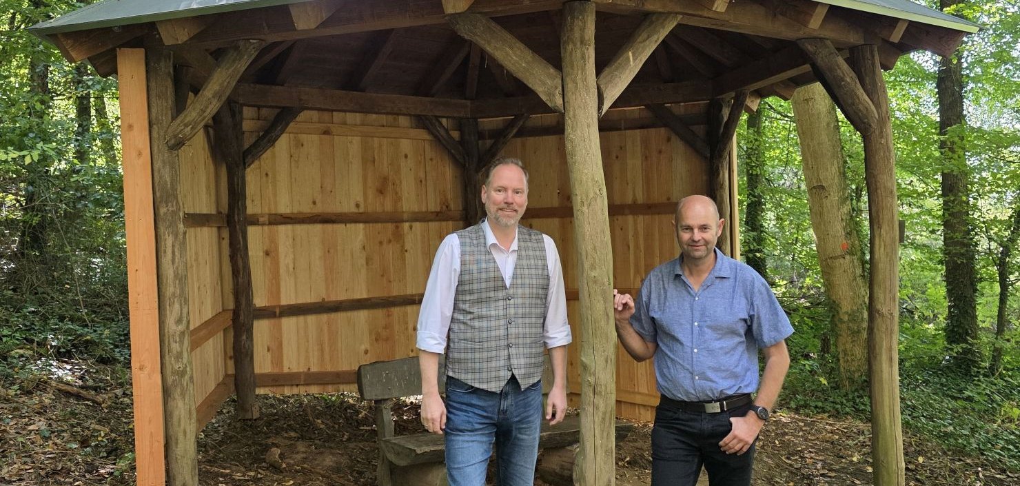 Bürgermeister Christian Litzinger und Bauamtsmitarbeiter Thorsten Amend stehen zusammen vor der sanierten Wanderschutzhütte in Meerholz. 