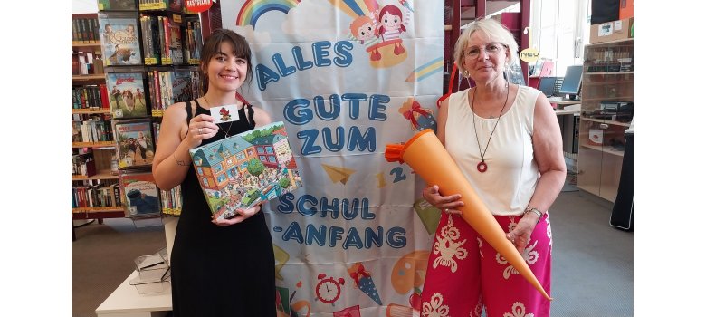Zwei Mitarbeiterinnen der Stadtbücherei stehen vor einem Schulanfangsplakat