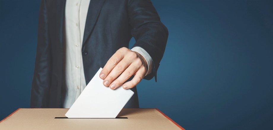 Ein Umschlag wird in eine Wahlurne geworfen. 