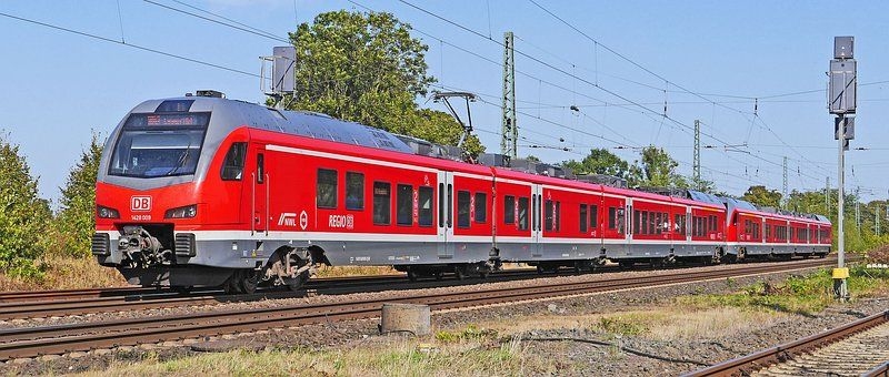 Bild einer roten Bahn auf Gleisen im Hintergrund sieht man Bäume. 
