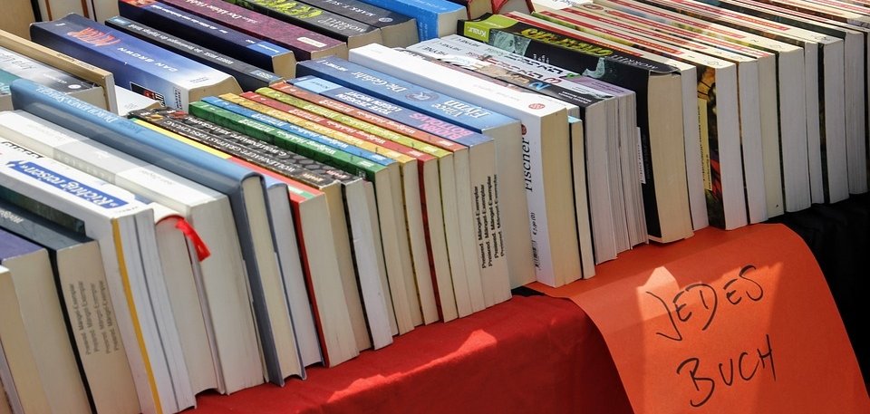 Das Bild zeigt einen Flohmarkttisch mit einer roten Tischdecke auf dem mehrere Bücher liegen. 