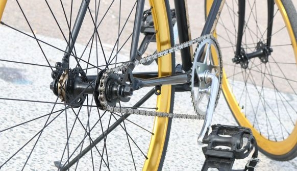 Nahaufnahme eines gelben Fahrrads, zusehen ist der untere Teil eines Fahrrads mit den Pedalen und der Kette. 